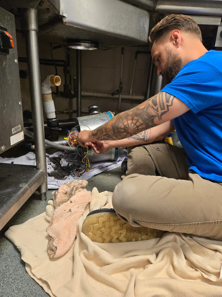Justin replacing a garbage disposal under a stainless kitchen sink